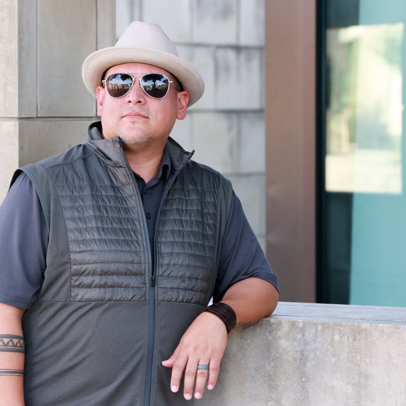 Frontman in a fedora and vest leaning on a wall